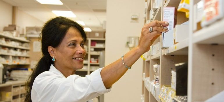 A woman doctor reaching to get medicine necessary for benzo detox Florida from the shelf.