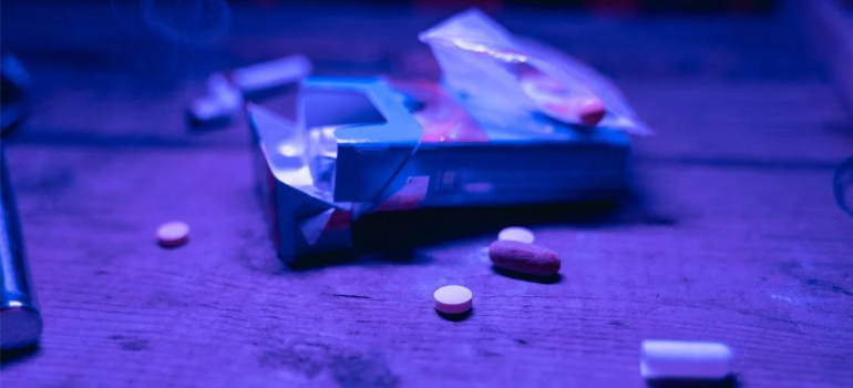 A close-up of an empty pack of cigarettes next to drug pills on a wooden table.