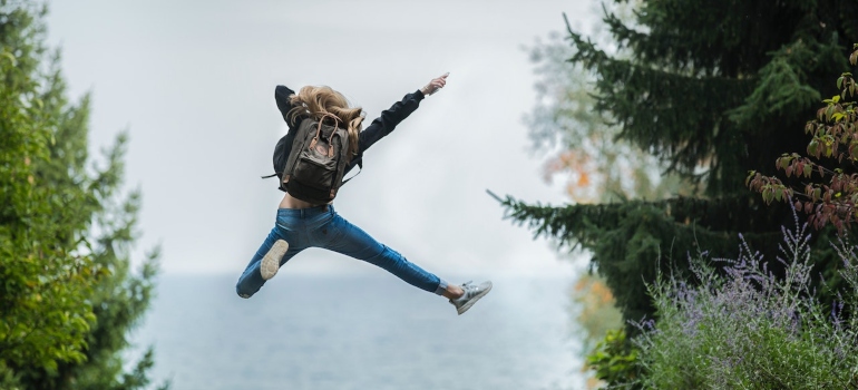A woman with a backpack jumping excitedly.