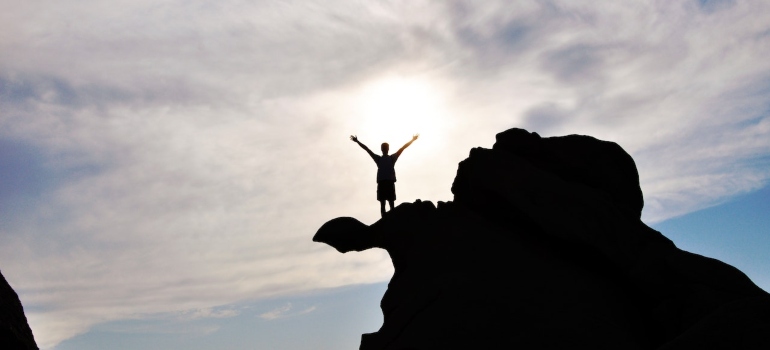 A silhouette of a person standing on top of a rocky formation.
