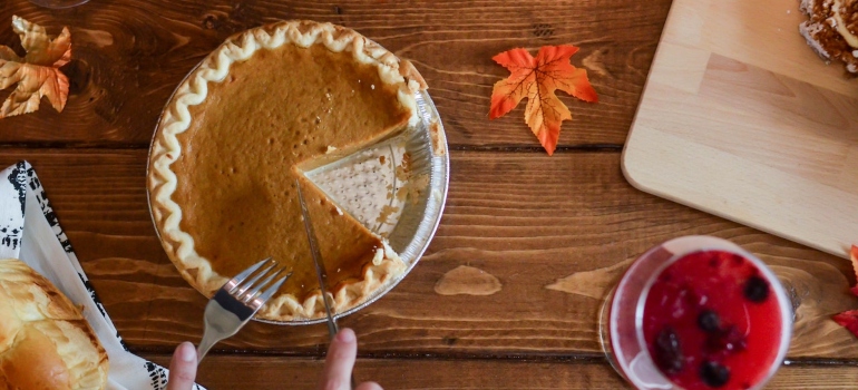 A person cutting pumpkin pie they made following the guide to cooking Thanksgiving dinner stress free.