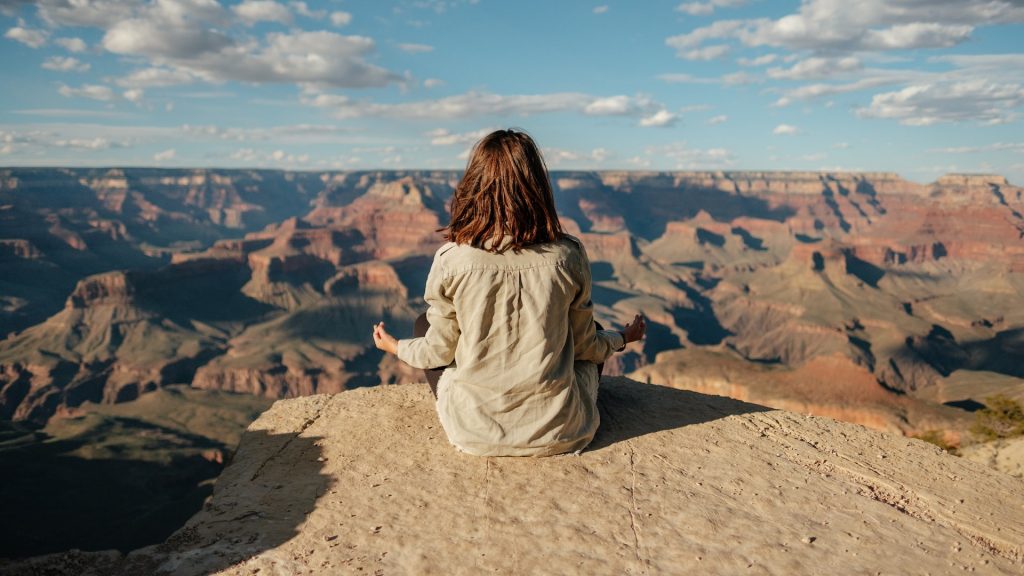 Photo of a woman meditating at the Grand Canyon as a featured image for post about stress relievers to do before you start your day sober