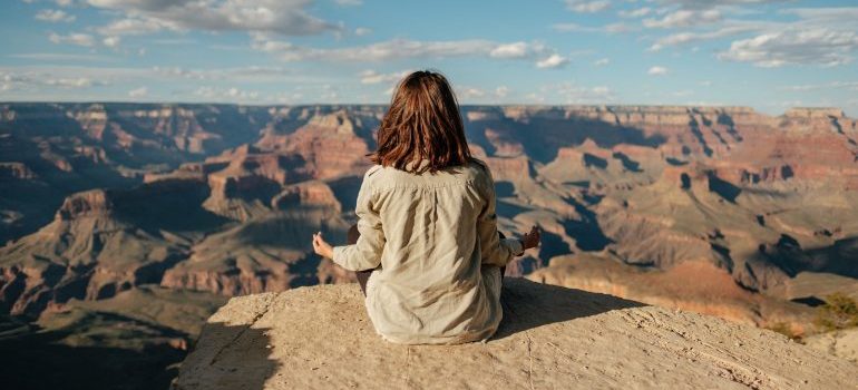 Photo of a woman meditating at the Grand Canyon as a featured image for post about stress relievers to do before you start your day sober