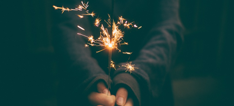 A close-up of a woman in a sweater holding a lit sparkler.