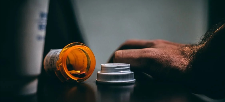 A close-up of a man’s hand on a counter next to an open bottle of medical pills.