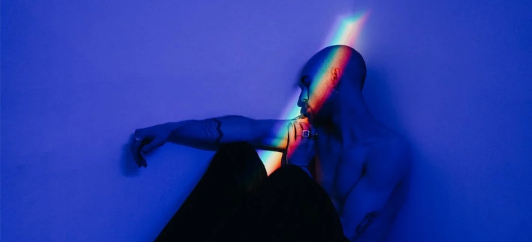 A depressed young man lying in bed with a rainbow-colored light shining on his face.