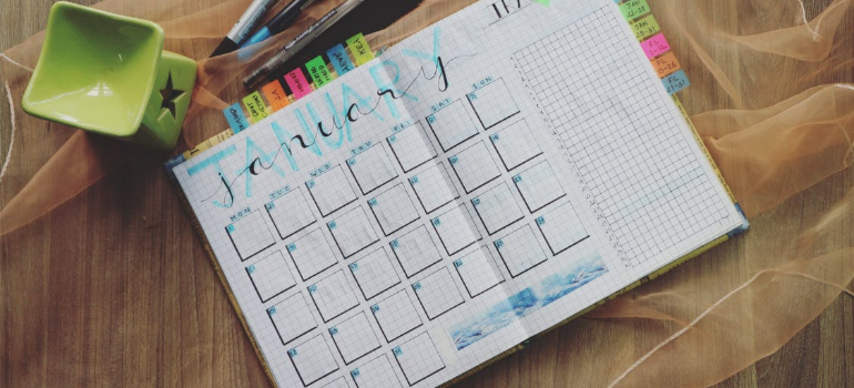 A calendar and planner on a wooden surface by pens.