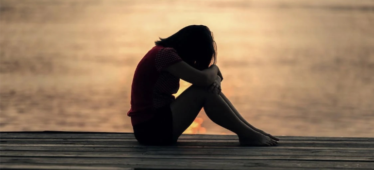 The silhouette of a depressed young woman sitting by a body of water representing polydrug abuse facts