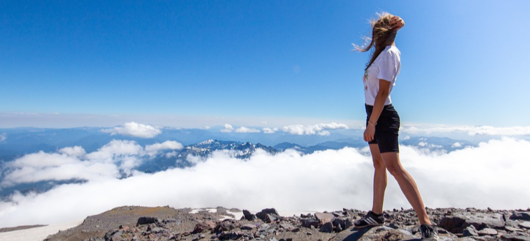 A woman on a mountain top enjoying the view of clouds underneath representing celebrating sobrierty milestones