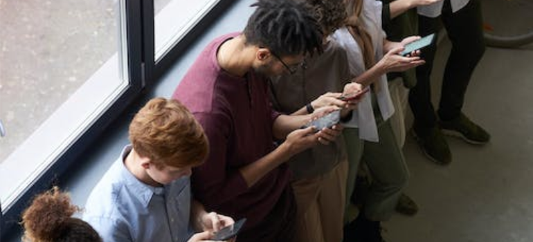 A row of young people leaning on a wall and using smartphones.