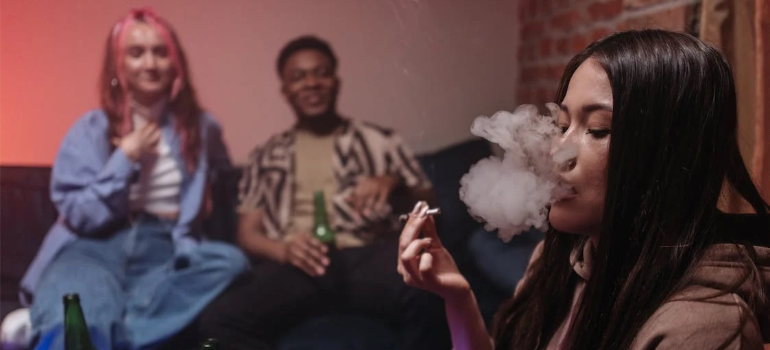 A group of young individuals smoking marijuana and drinking alcohol indoors.