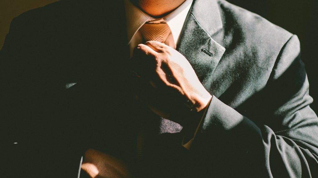 A man in a business suit adjusting his tie.