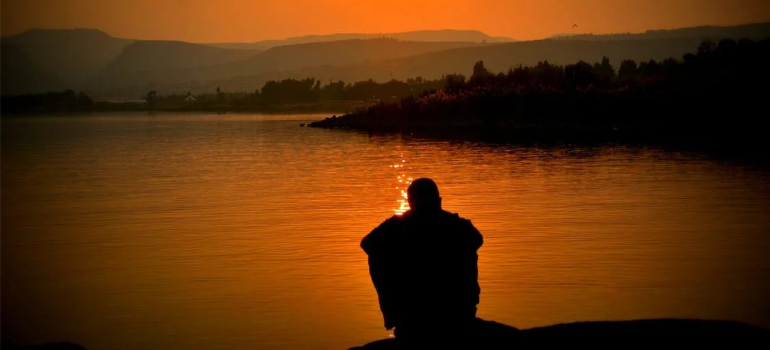 A person sitting by a body of water at dusk.