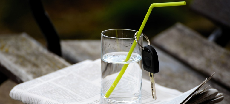 A glass of water with a green straw which has car keys hanging from it.