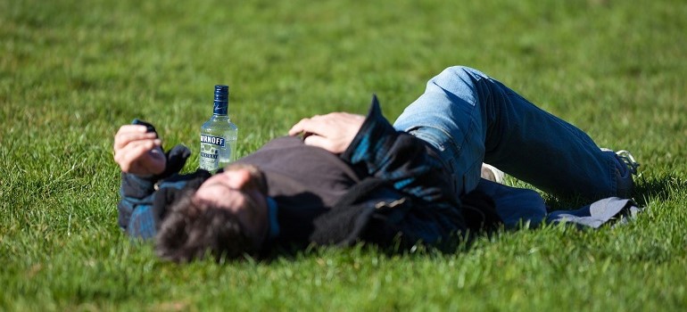 Man laying on grass with a bottle of alcohol.