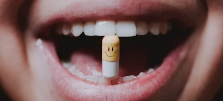 A close-up of a woman holding a pill in her teeth, illustrating the urgency of minimizing the negative consequences of drug use.