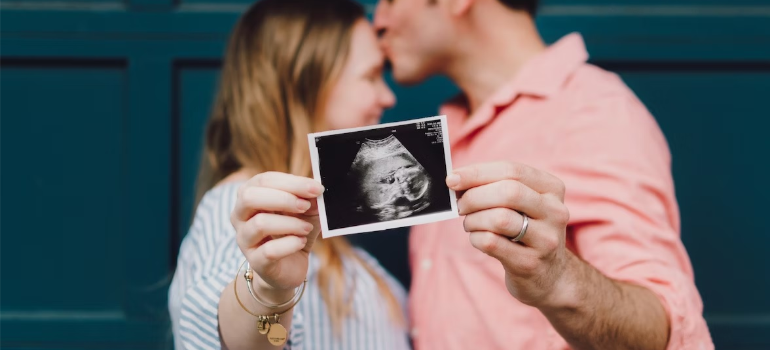 A happy couple holding a baby scan photo.