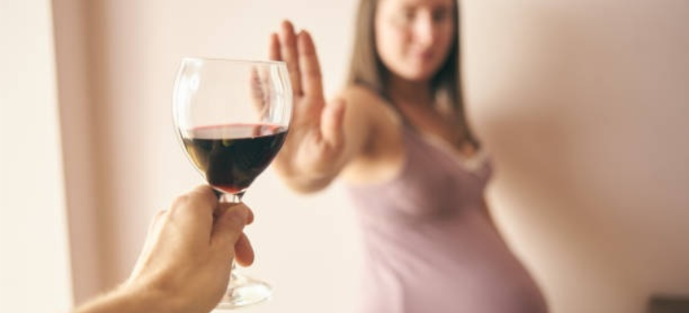 A pregnant woman refusing a glass of wine, illustrating how there is no amount of acceptable alcohol during pregnancy.